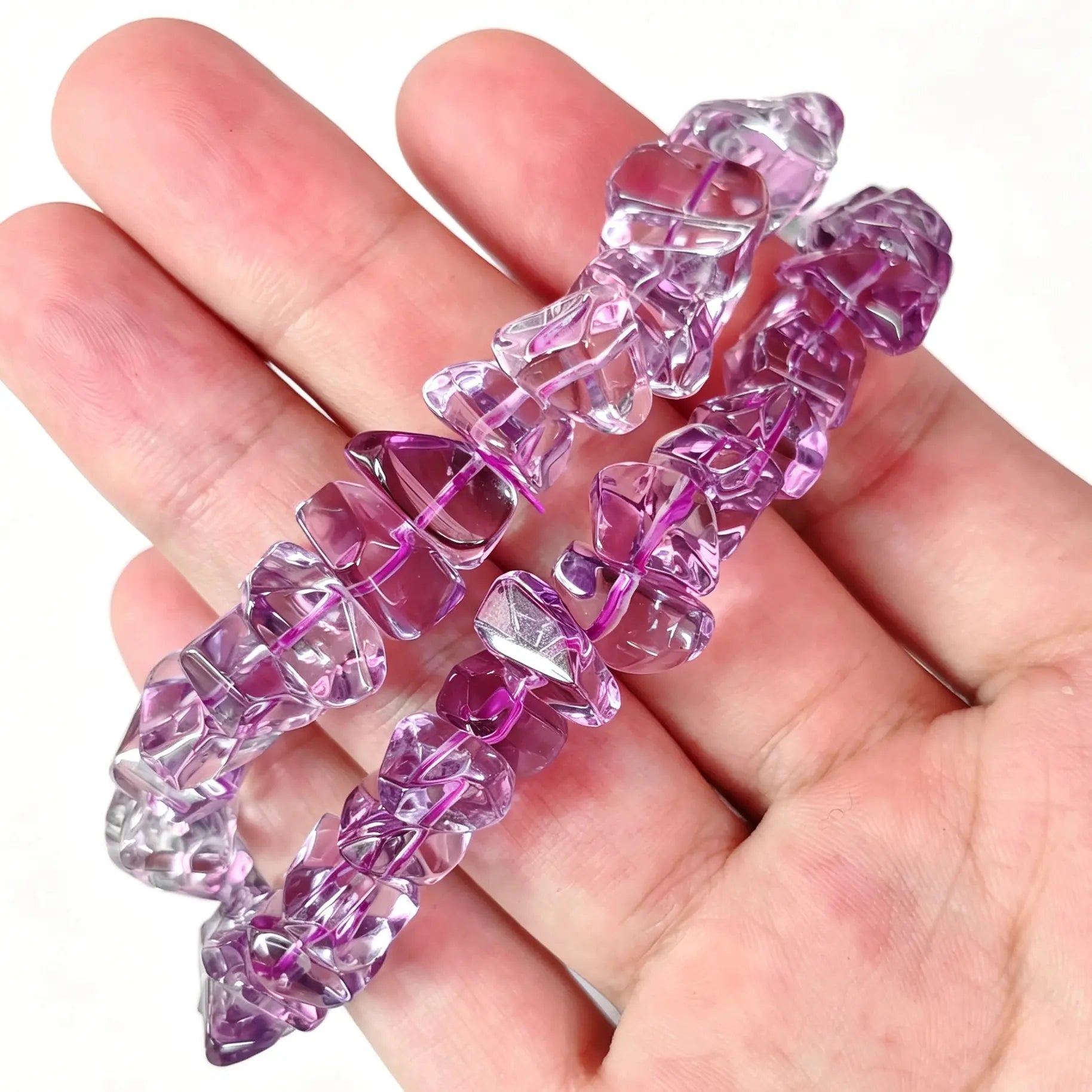 Main view of stacked high clarity amethyst freeform chip bracelets resting on open palm showing bright purple transparency