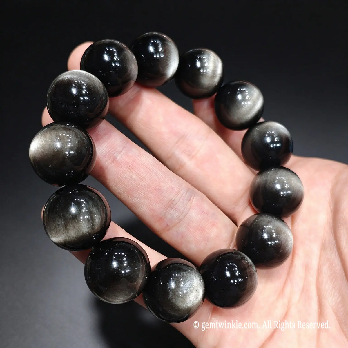 High end chatoyant double eye silver obsidian bracelet held in hand showcasing crisp reflective lines