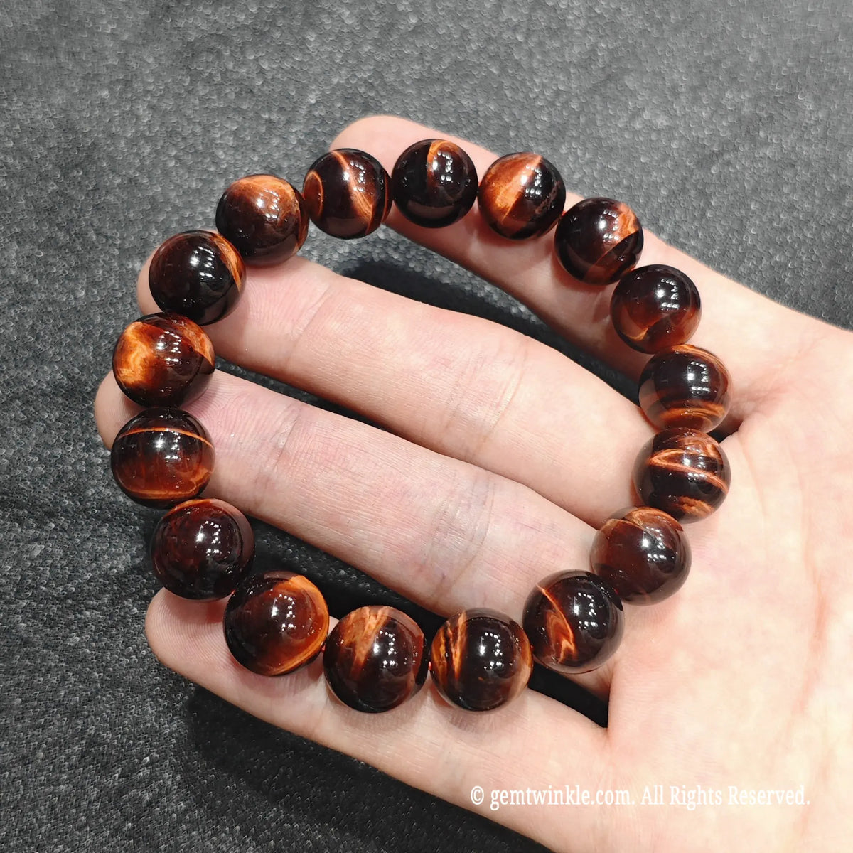 Full circle view of a premium red tiger eye stretch bracelet resting on hand showing glossy finish and deep crimson tone