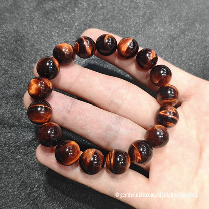 Full circle view of a premium red tiger eye stretch bracelet resting on hand showing glossy finish and deep crimson tone
