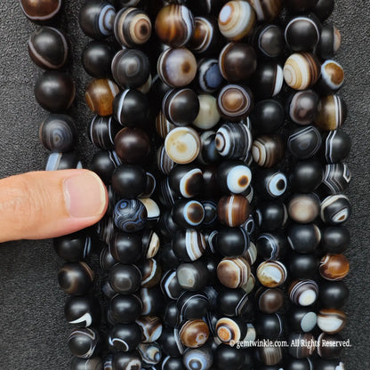 hand holding a large wholesale bundle of high quality gemstone beads in frosted black eye agate for boutique store sourcing