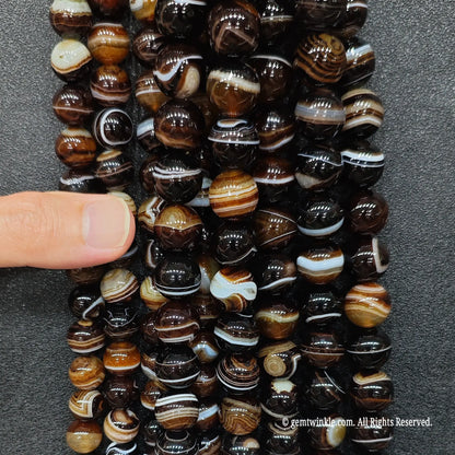 hand holding a massive wholesale bundle of high quality gemstone beads in dyed grey banded agate for crystal store inventory sourcing