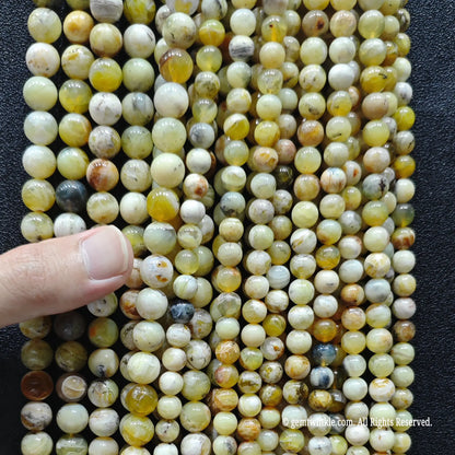 hand holding a massive bundle of high quality gemstone beads in natural yellow opal matrix showing stock volume for boutique retail sourcing