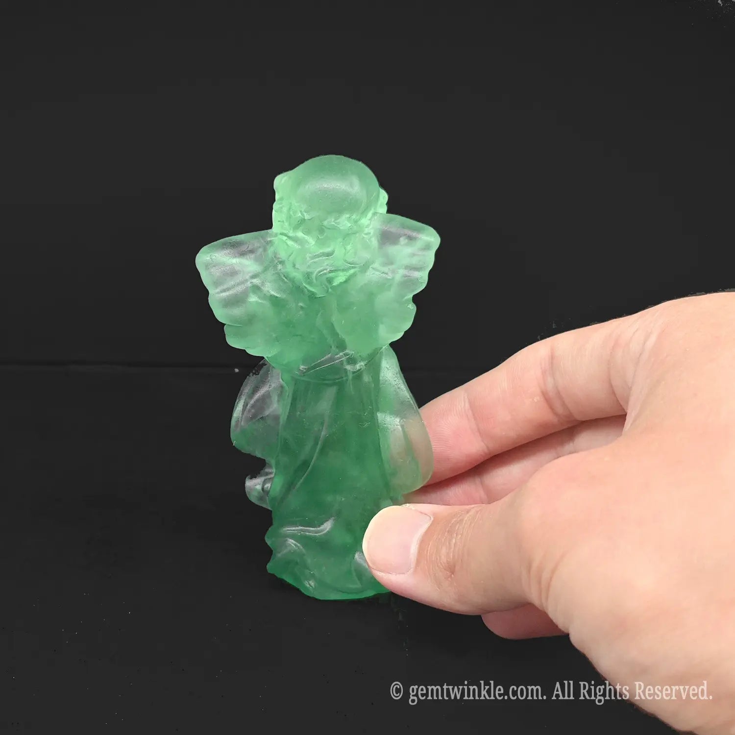 Hand holding an approx 10cm green fluorite praying angel carving to demonstrate the exact product scale and pocketsize comfort for crystal healing buyers