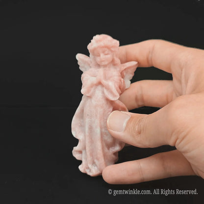 Hand holding an approx 10cm pink opal praying angel carving showing its exact physical scale and soft rose-pink color for crystal buyers