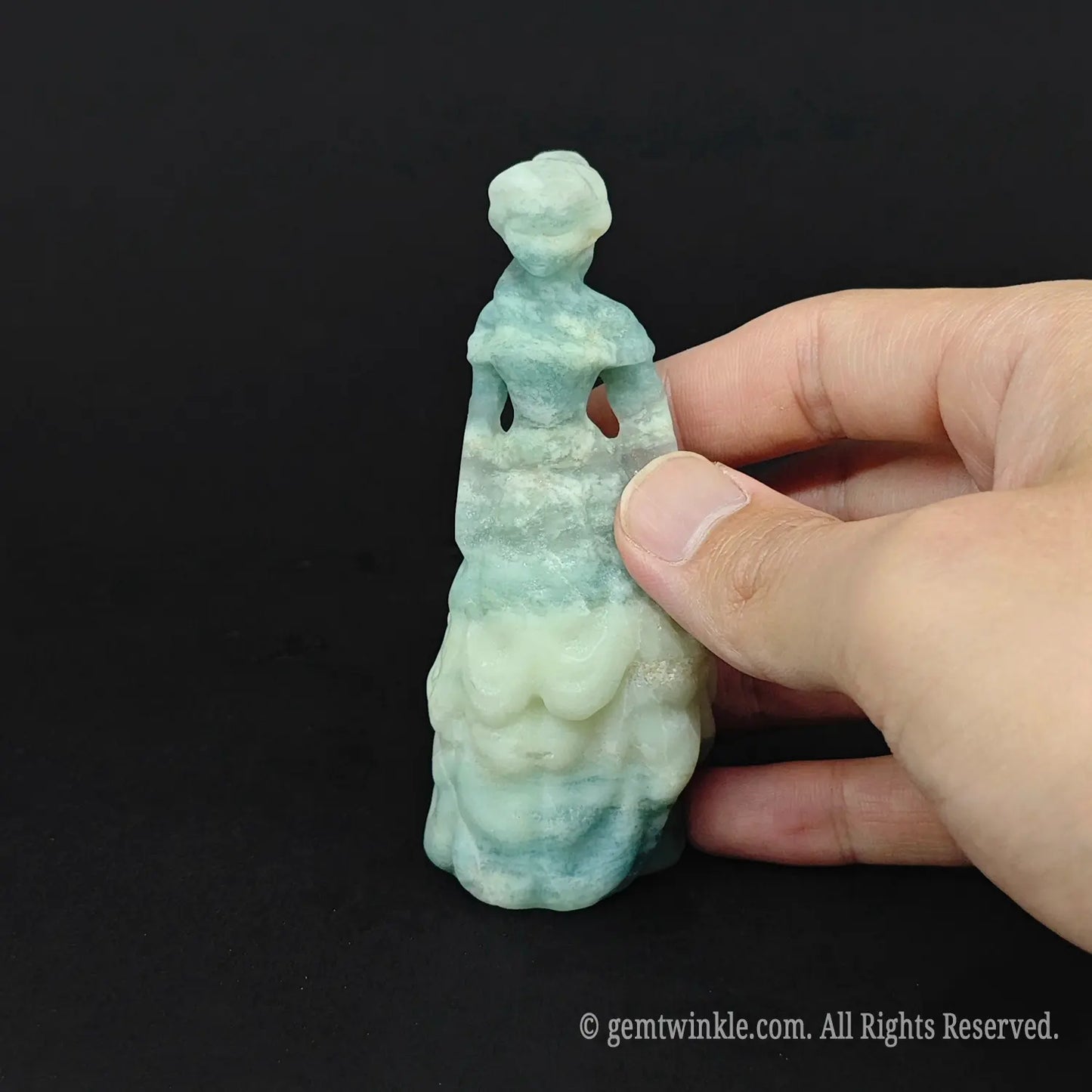 Hand holding an approx 10cm (4 inches) natural ocean banded crystal princess statue to display its waxy luster and actual size for wholesale buyers