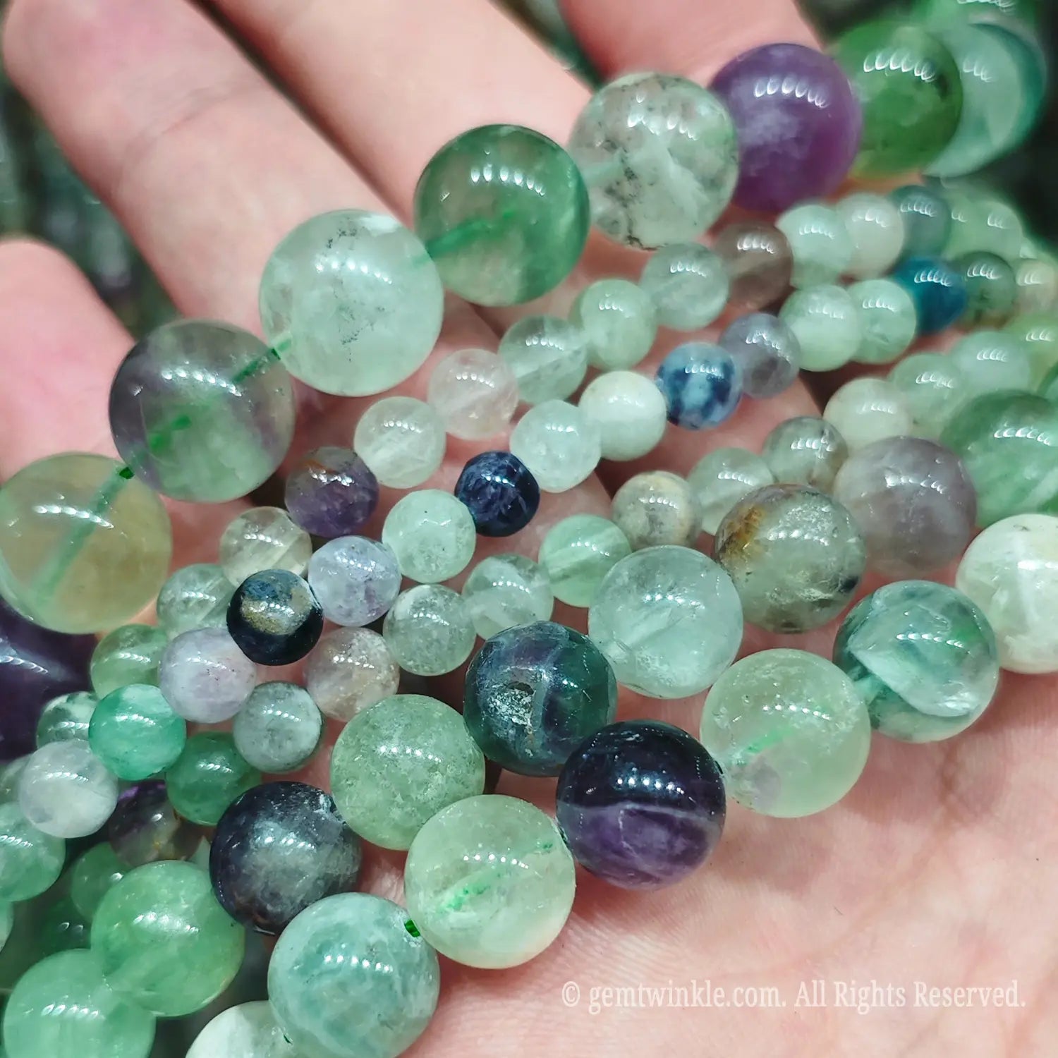 Hand holding various sizes of natural feather fluorite crystal strands under bright light to display clarity and floating feather patterns