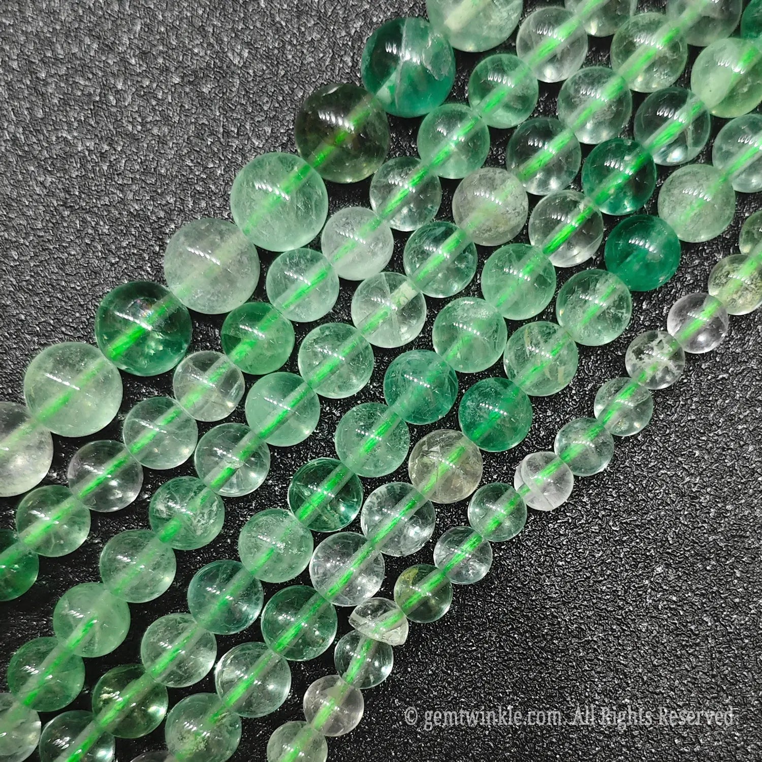 Hand holding Grade B natural green fluorite loose beads strands showing beautiful internal ice cracks and organic cotton structures under natural light