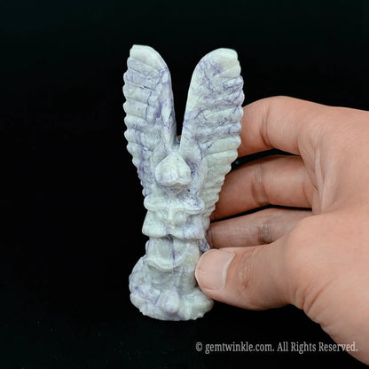 Hand holding a ten centimeter purple zebra stone angel wings statue to display actual scale and natural striped lines