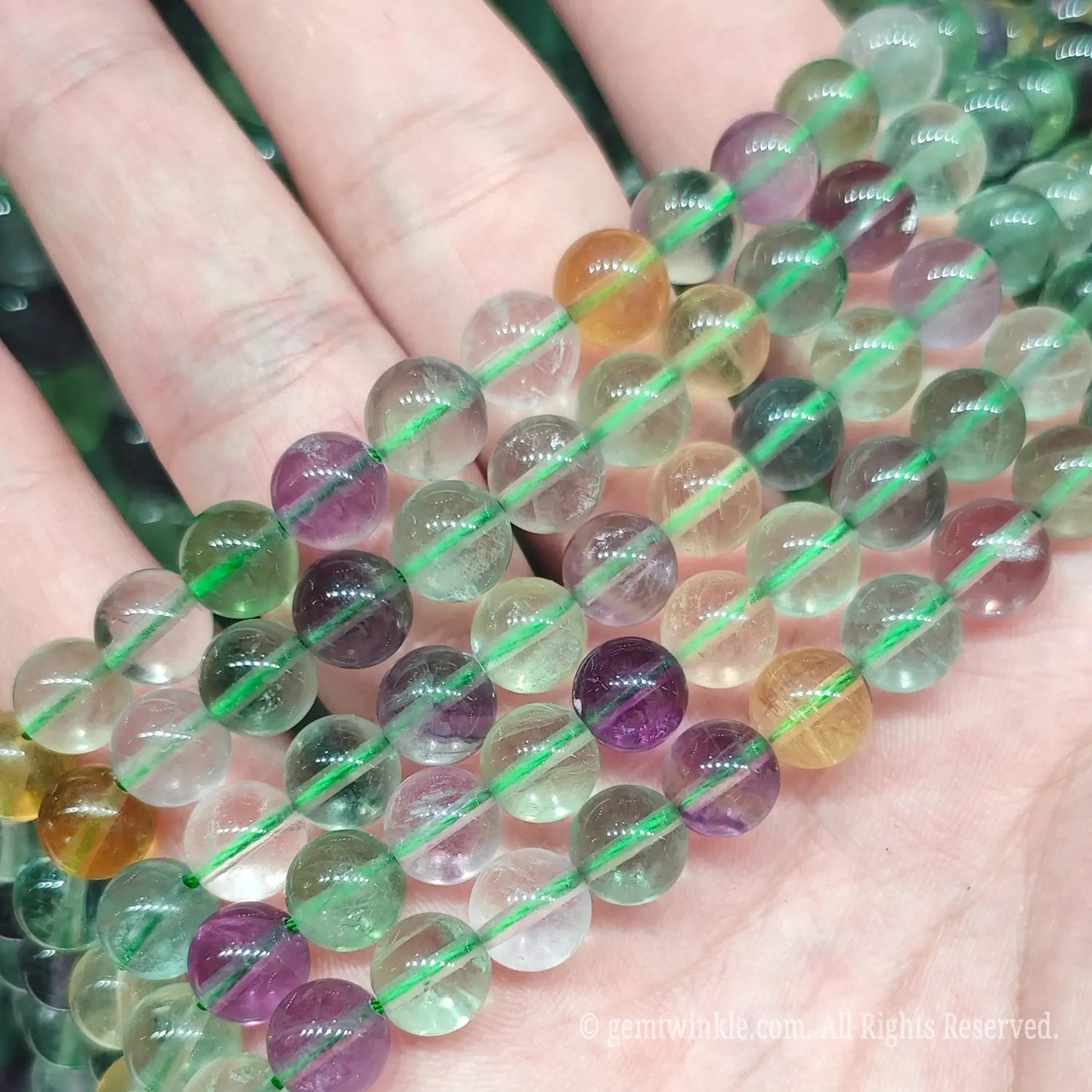 Hand holding colorful natural rainbow fluorite gemstone loose beads strands under natural light for handcrafted jewelry designers and Etsy creators