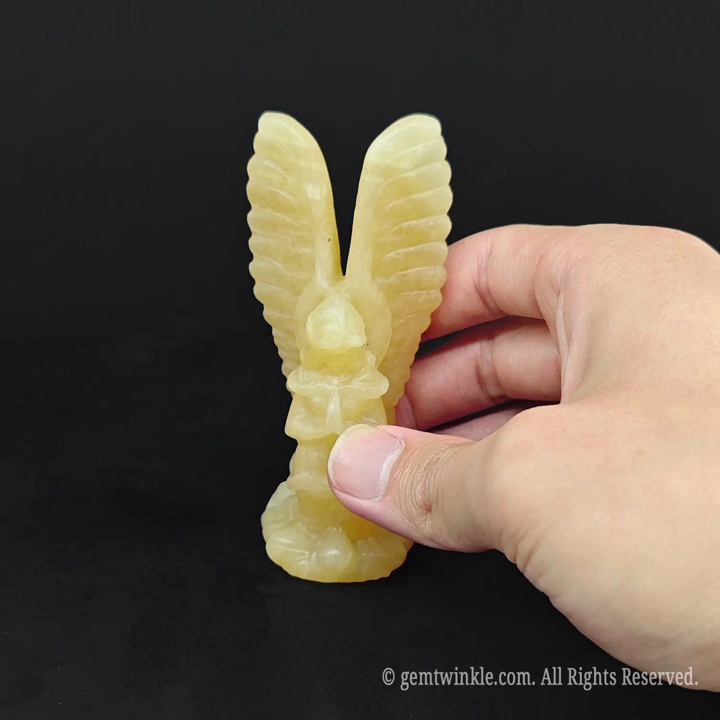 Hand holding a yellow calcite angel sculpture showing its smooth matte natural stone luster