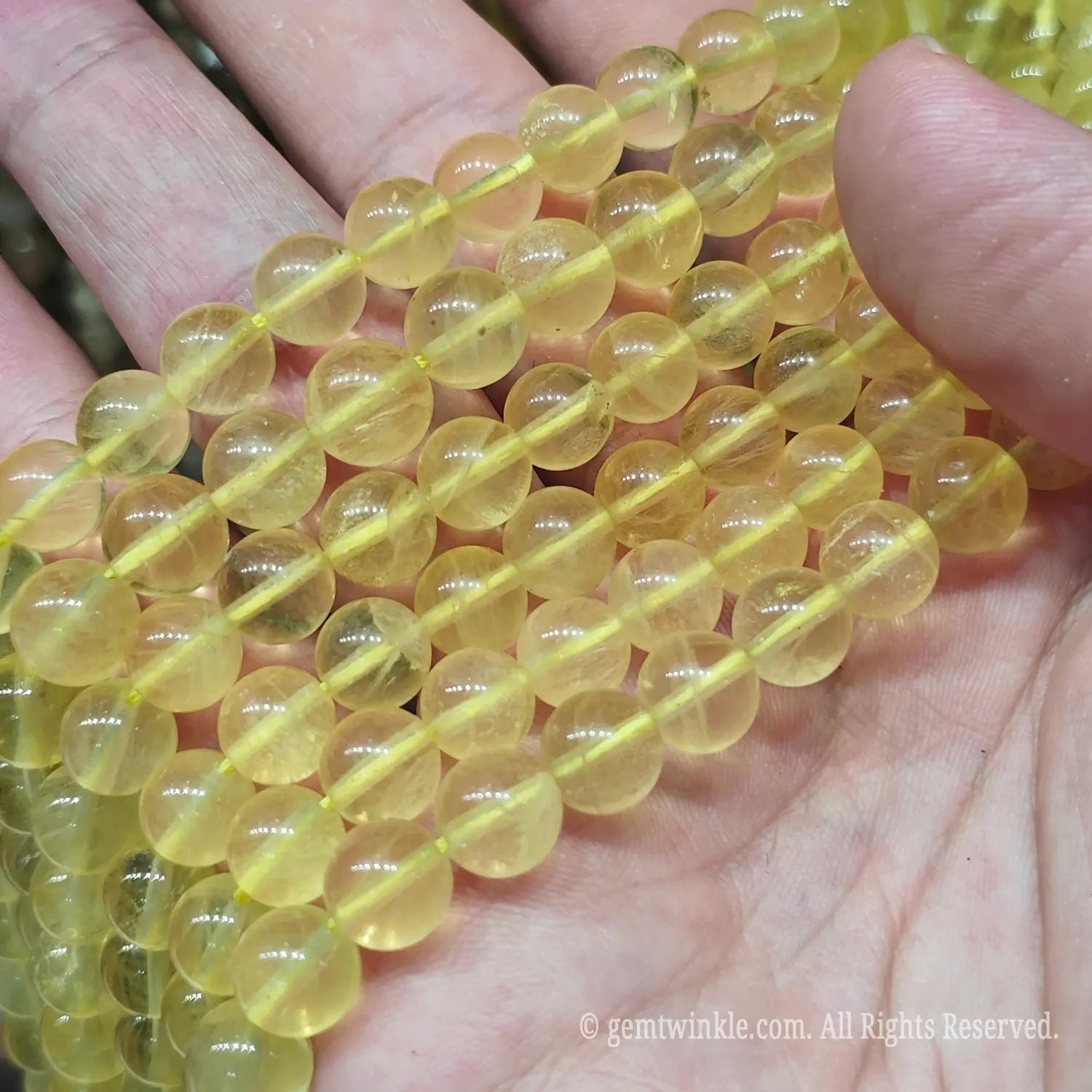 Hand holding translucent golden yellow fluorite loose beads strands under warm light for boutique jewelry designers and Etsy creators.