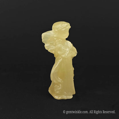 Side view of a hand-carved natural honey calcite angel figurine showcasing detailed wings, flowing robes, and rich golden mineral tones