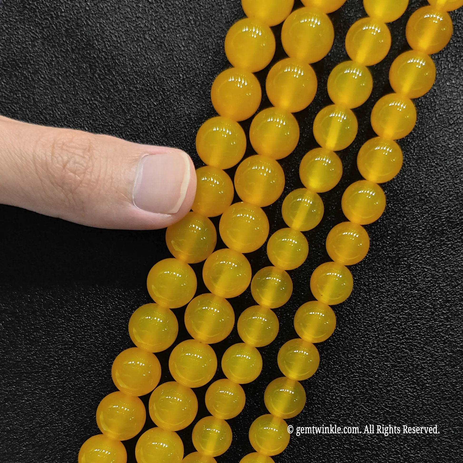 Pointing to multiple strands of glossy honey yellow agate crystal loose beads for scale verification