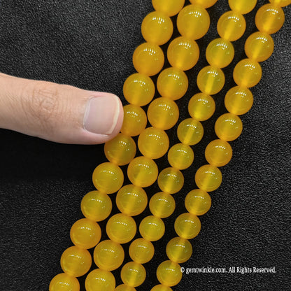 Pointing to multiple strands of glossy honey yellow agate crystal loose beads for scale verification