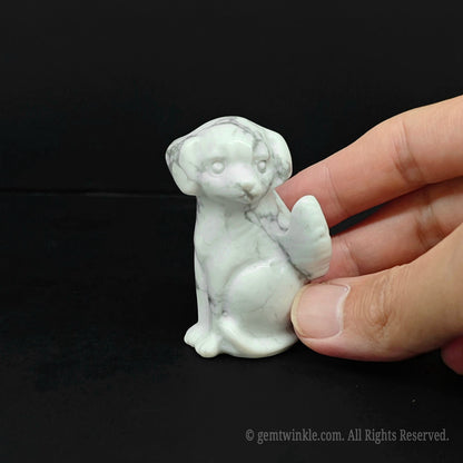 Front view of a 6cm white howlite gemstone angel dog figurine with delicate dark veins resting on a black surface