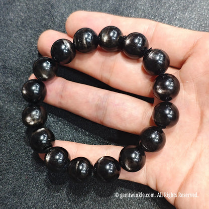 Full circle view of a natural hypersthene bead stretch bracelet resting on hand showing glossy finish