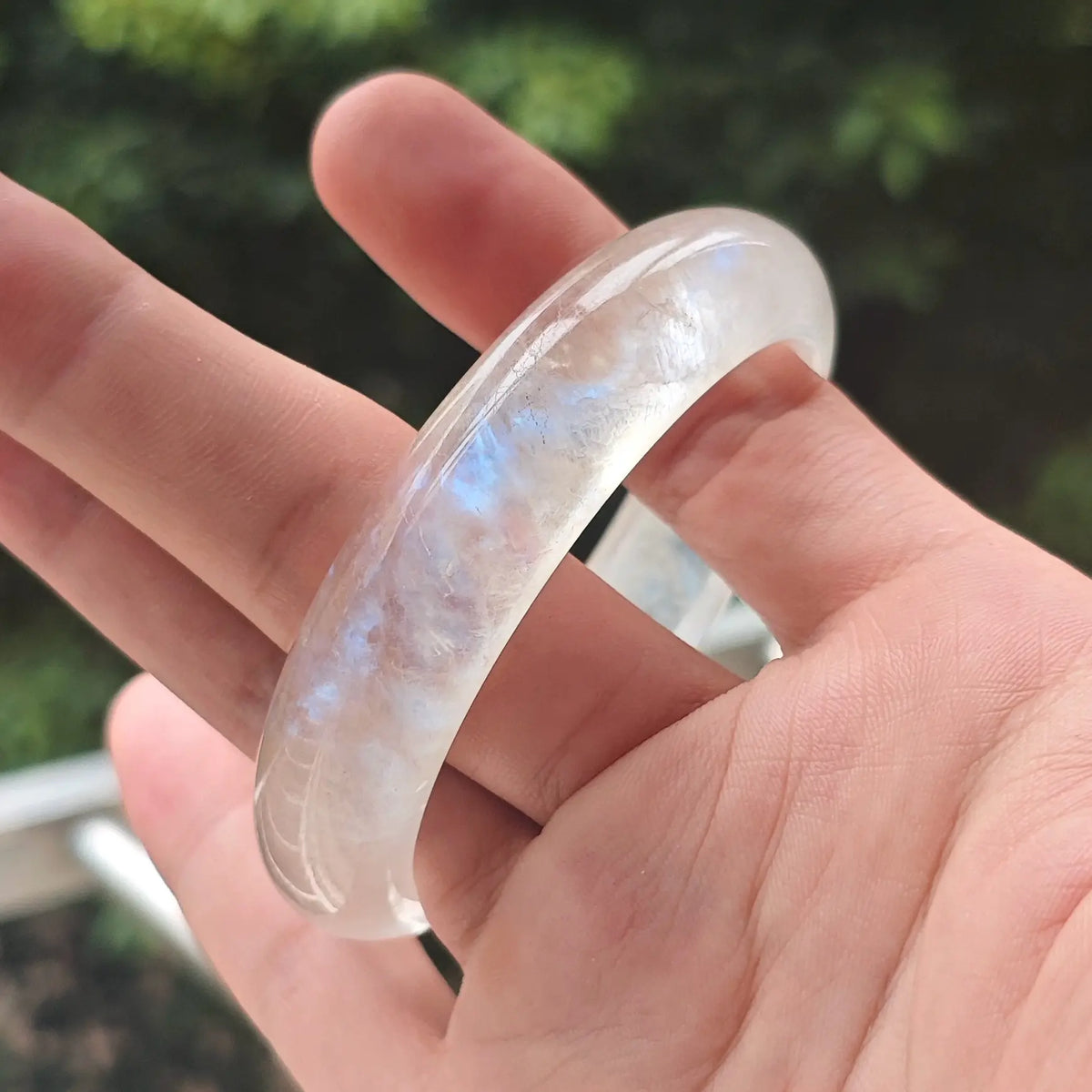 Hand holding a natural ice-grade blue moonstone bangle showcasing strong electric blue flash for wholesale buyers