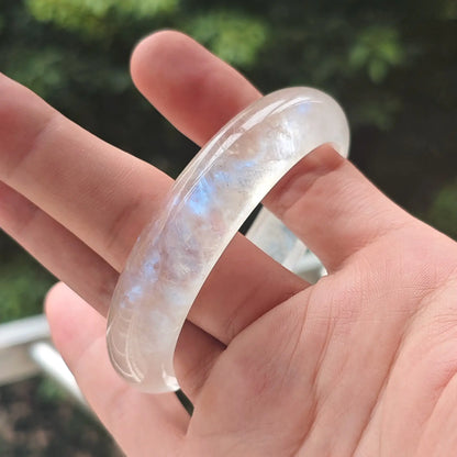 Hand holding a natural ice-grade blue moonstone bangle showcasing strong electric blue flash for wholesale buyers
