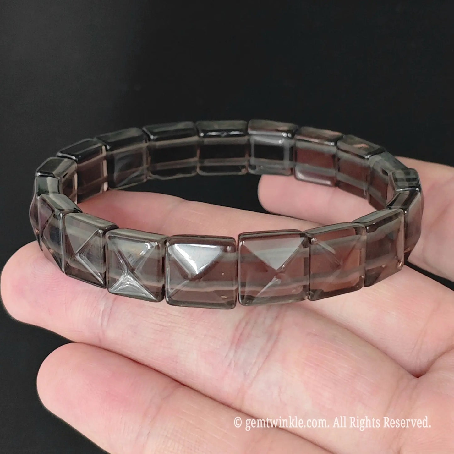 Overview of ice obsidian geometric pyramid cut 11mm square bead bracelet resting on fingers