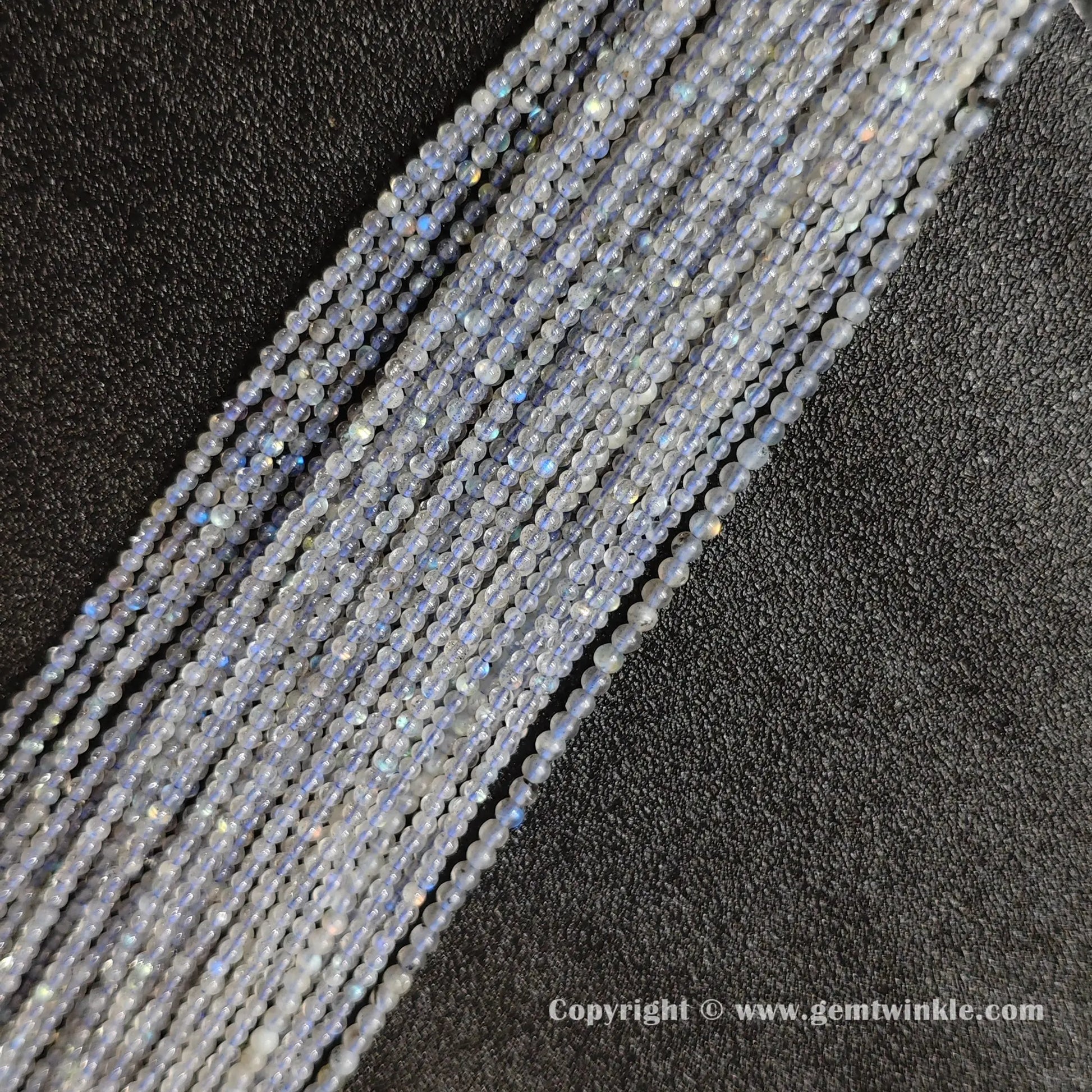 Angled display of icy grey blue moonstone micro seed bead strands glowing with intense blue optical shimmer