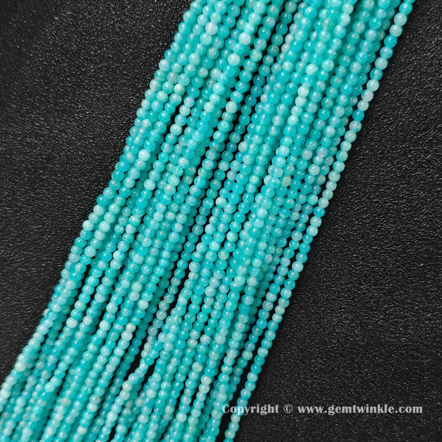 Multiple strands of icy seafoam natural amazonite 3mm micro seed beads aligned on dark leather background