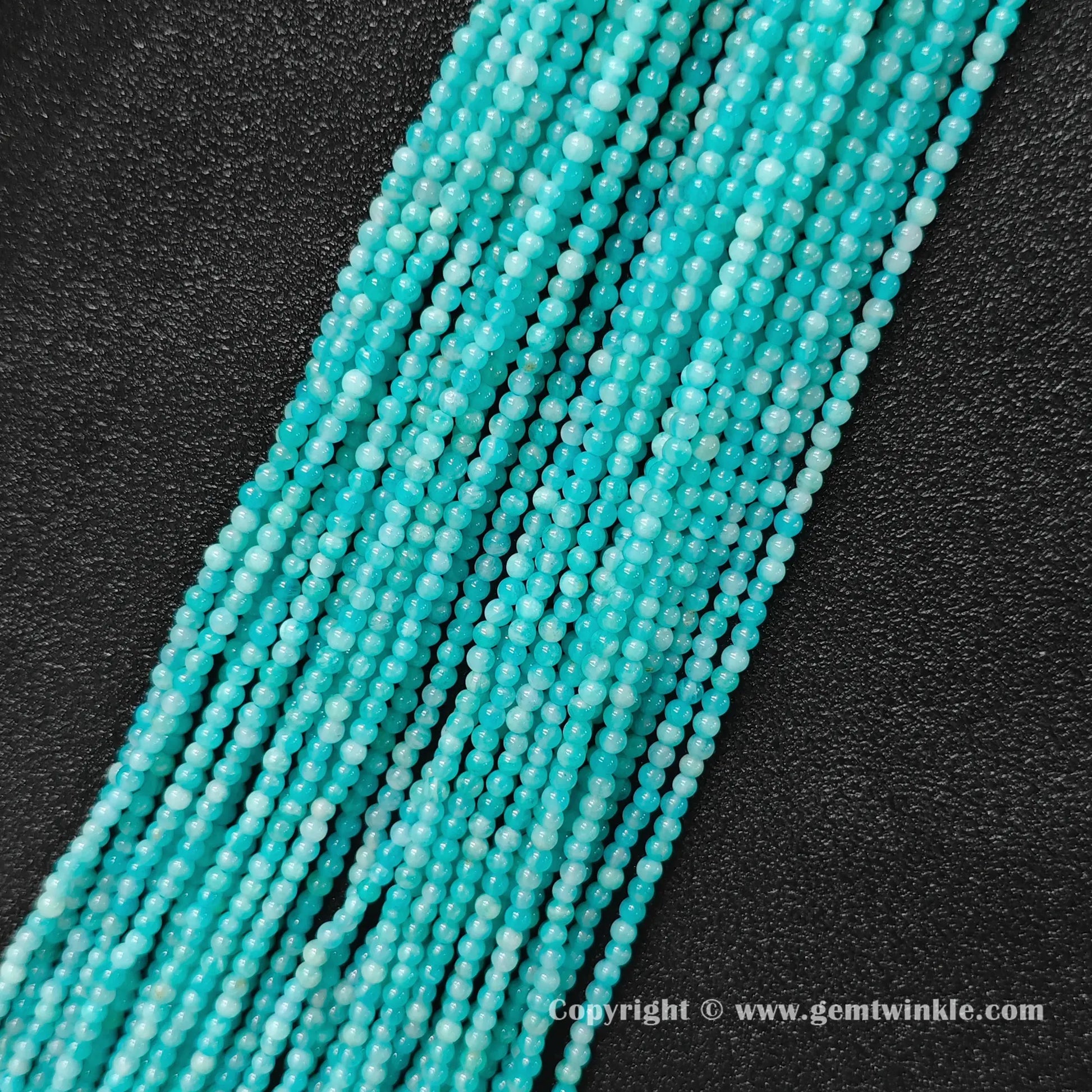 Multiple strands of icy seafoam natural amazonite 3mm micro seed beads aligned on dark leather background