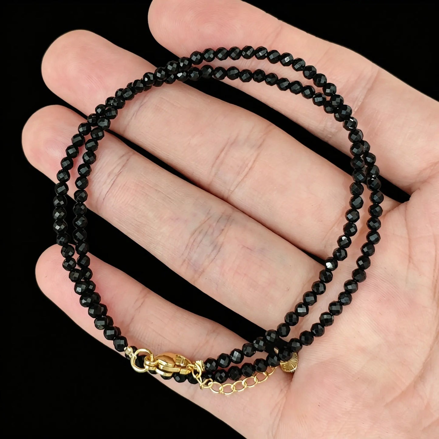 jet black tourmaline micro faceted bead strand held in hand with gold clasp