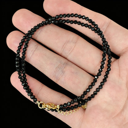 jet black tourmaline micro faceted bead strand held in hand with gold clasp