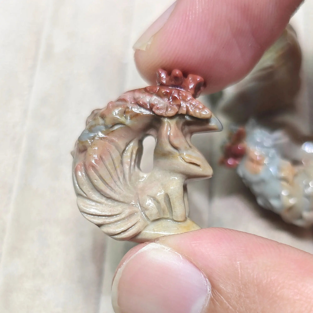 Close up view of a mini celestial fox carving with terracotta pink and golden highlights held in hand