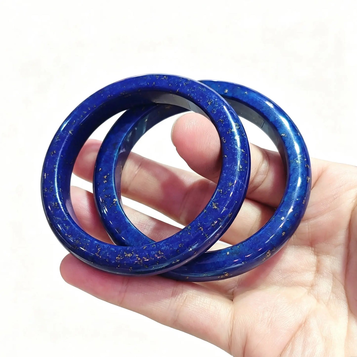 Pair of smooth round lapis lazuli solid gemstone bangles held in hand showing rich blue mineral texture