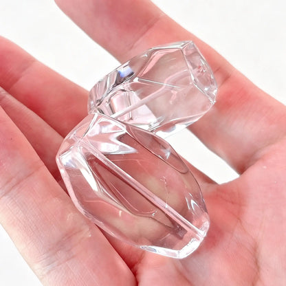 Main handheld view of two 30-35mm large clear quartz faceted freeform nugget beads showcasing ice clear clarity and center drilled hole