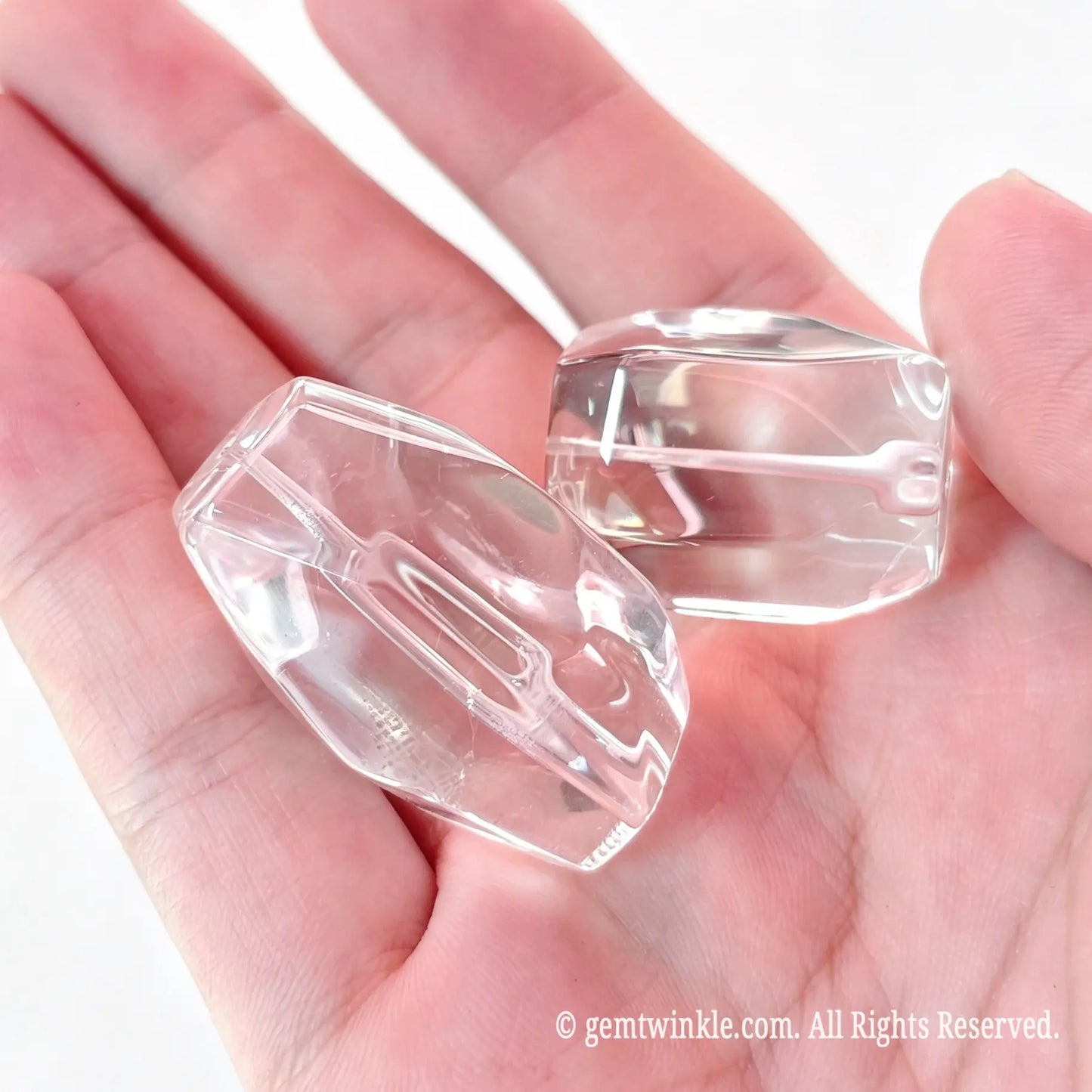 Palm view of two large natural rock crystal freeform faceted beads displaying geometric facets and drilled center holes