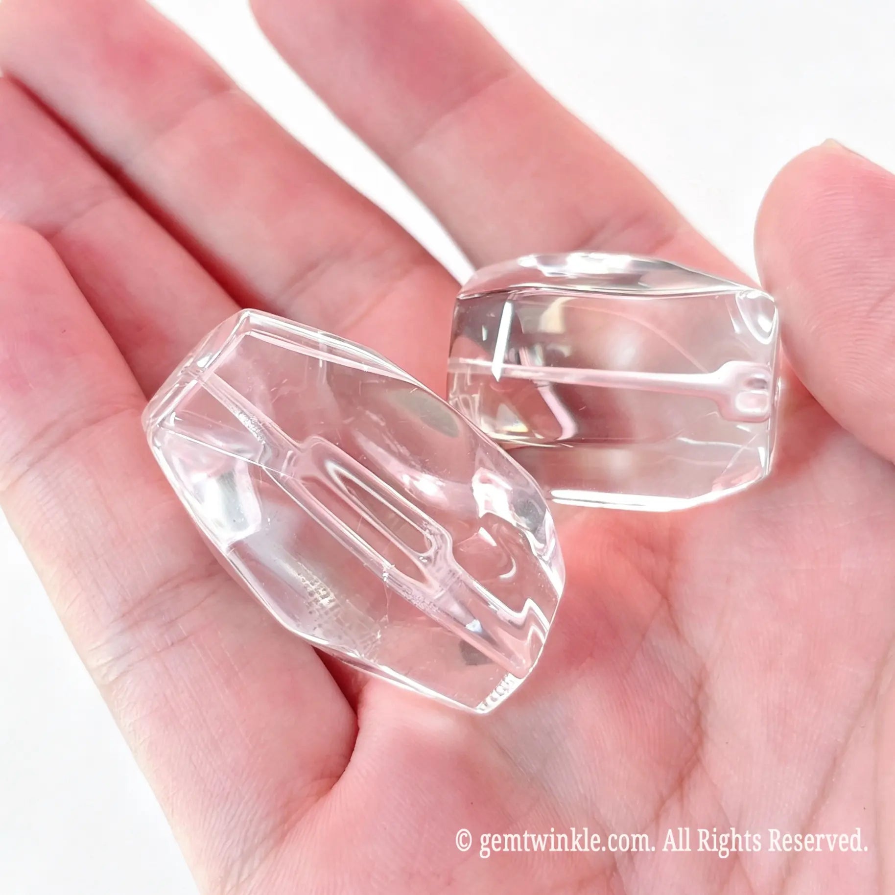 Palm view of two large natural rock crystal freeform faceted beads displaying geometric facets and drilled center holes
