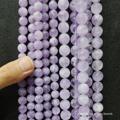 Hand holding multiple rows of natural lavender amethyst bead strands to demonstrate size scale and glossiness