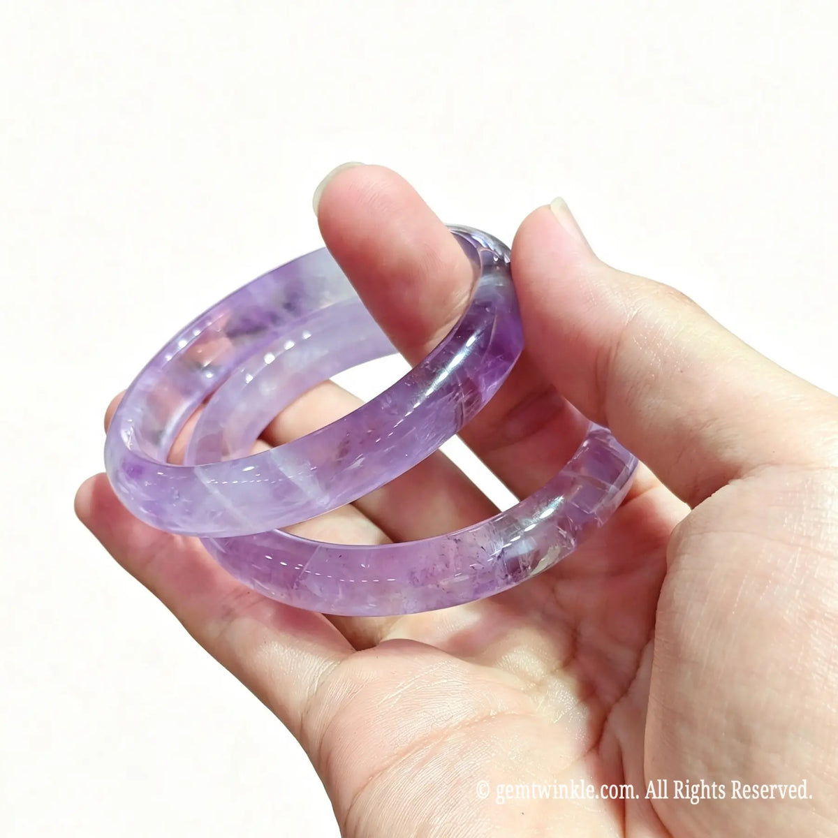 Hand holding two light purple amethyst bangles highlighting crystalline mist inclusions