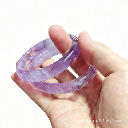 Hand holding two light purple amethyst bangles highlighting crystalline mist inclusions