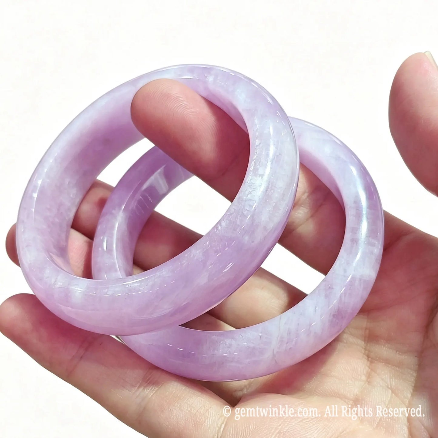 Pair of smooth round natural kunzite crystal bangles held in hand showing soft lilac purple color tone