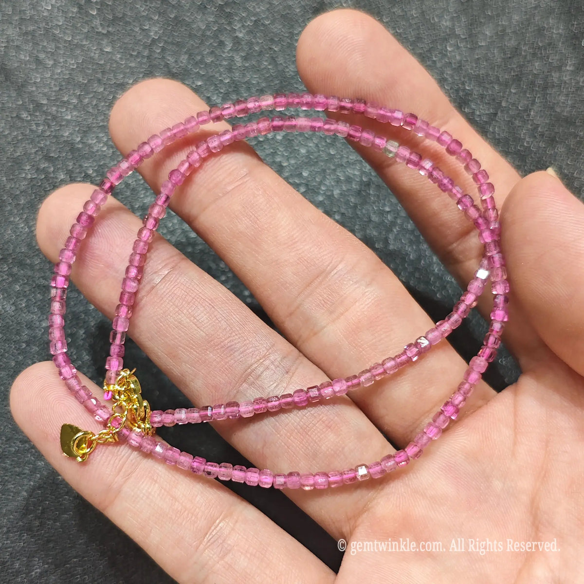Coiled 2.5mm geometric cube cut Pink Tourmaline necklace held across fingers suited for boutique store displays