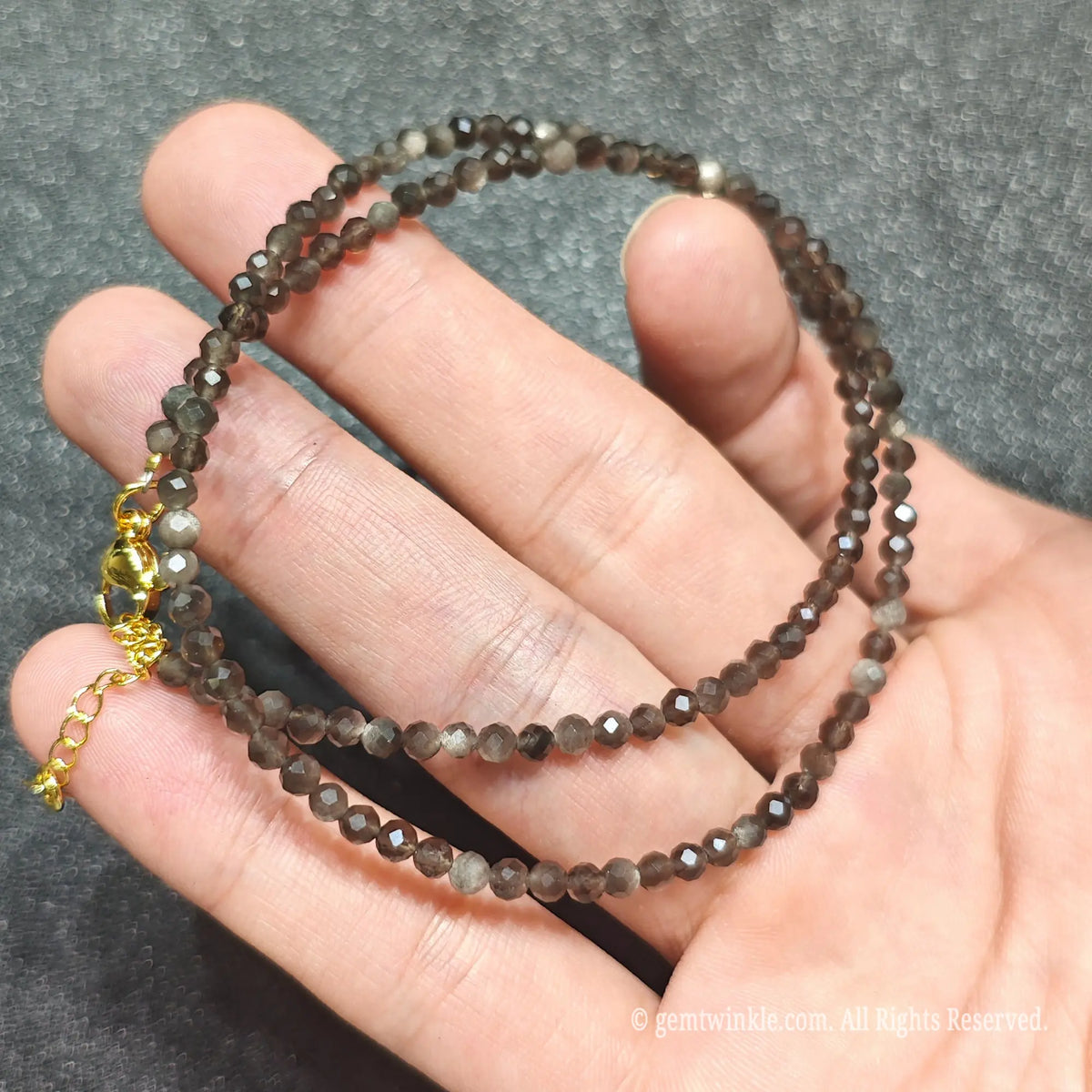 Coiled 3mm faceted Silver Sheen Obsidian necklace held across fingers suited for boutique reseller inventory