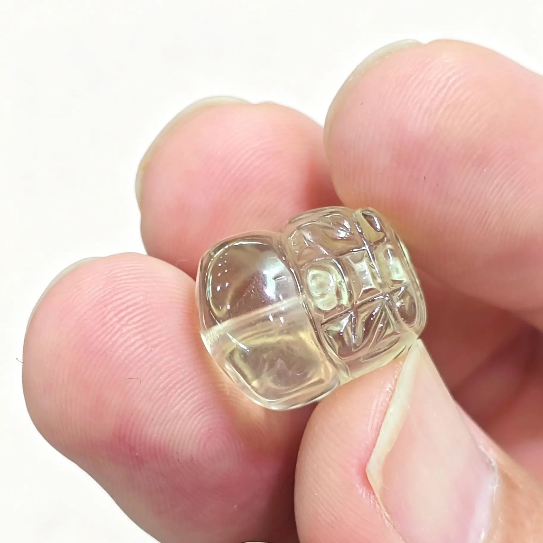 Lemon quartz carved Pixiu bead held between fingers showing detailed mythical creature relief and pale yellow clarity
