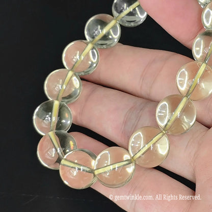 close up of clear yellow lemon quartz round bead strand across palm