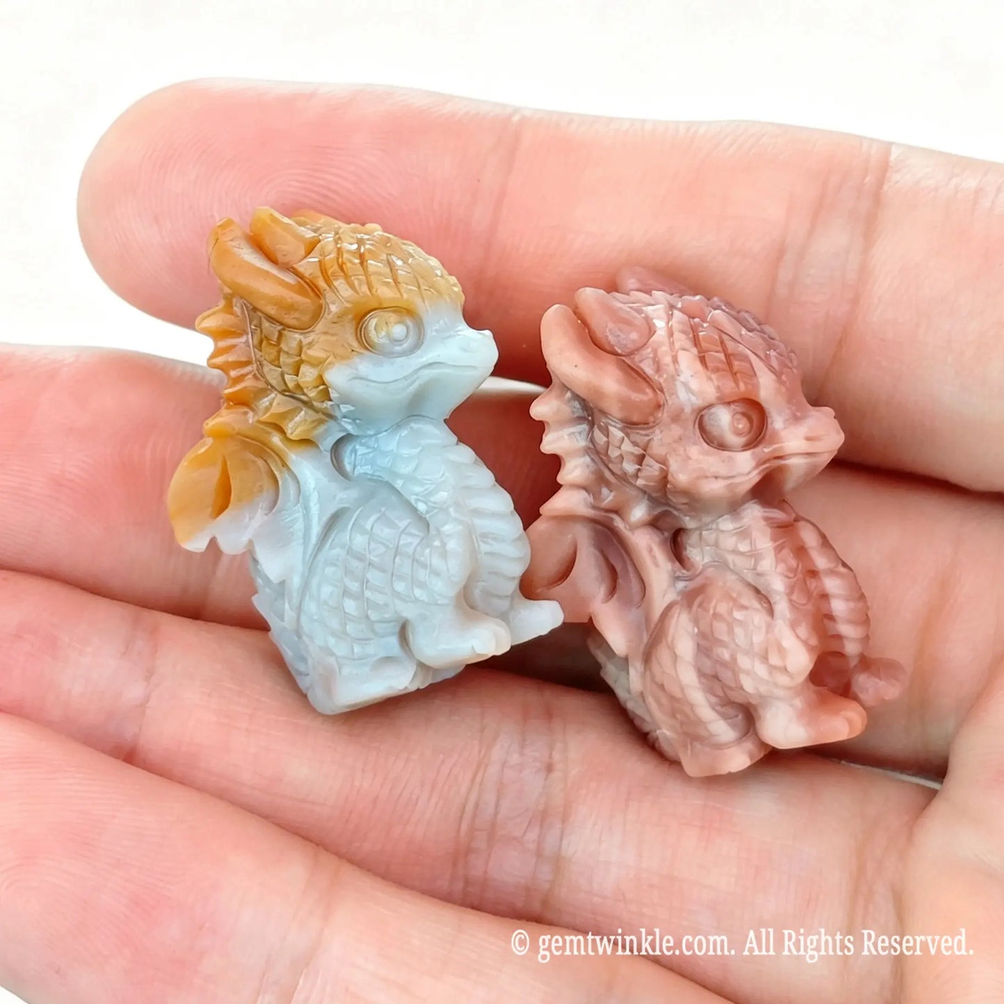 Handheld perspective of two 2.5cm Alashan agate carved little dragon figurines showing natural multi-tone chalcedony texture