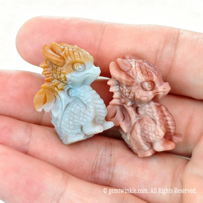 Handheld perspective of two 2.5cm Alashan agate carved little dragon figurines showing natural multi-tone chalcedony texture