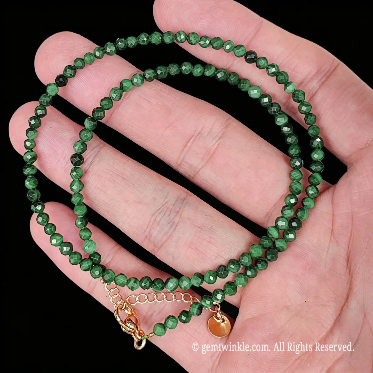 detail view of gold tone lobster clasp, extender chain and metal tag on malachite strand