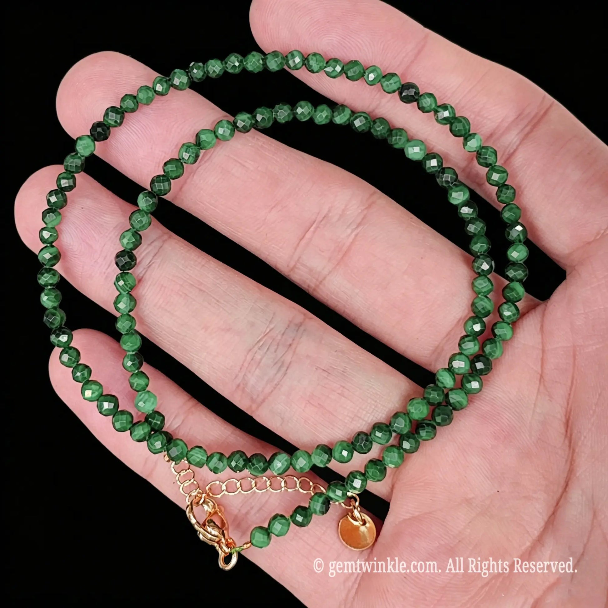 detail view of gold tone lobster clasp, extender chain and metal tag on malachite strand