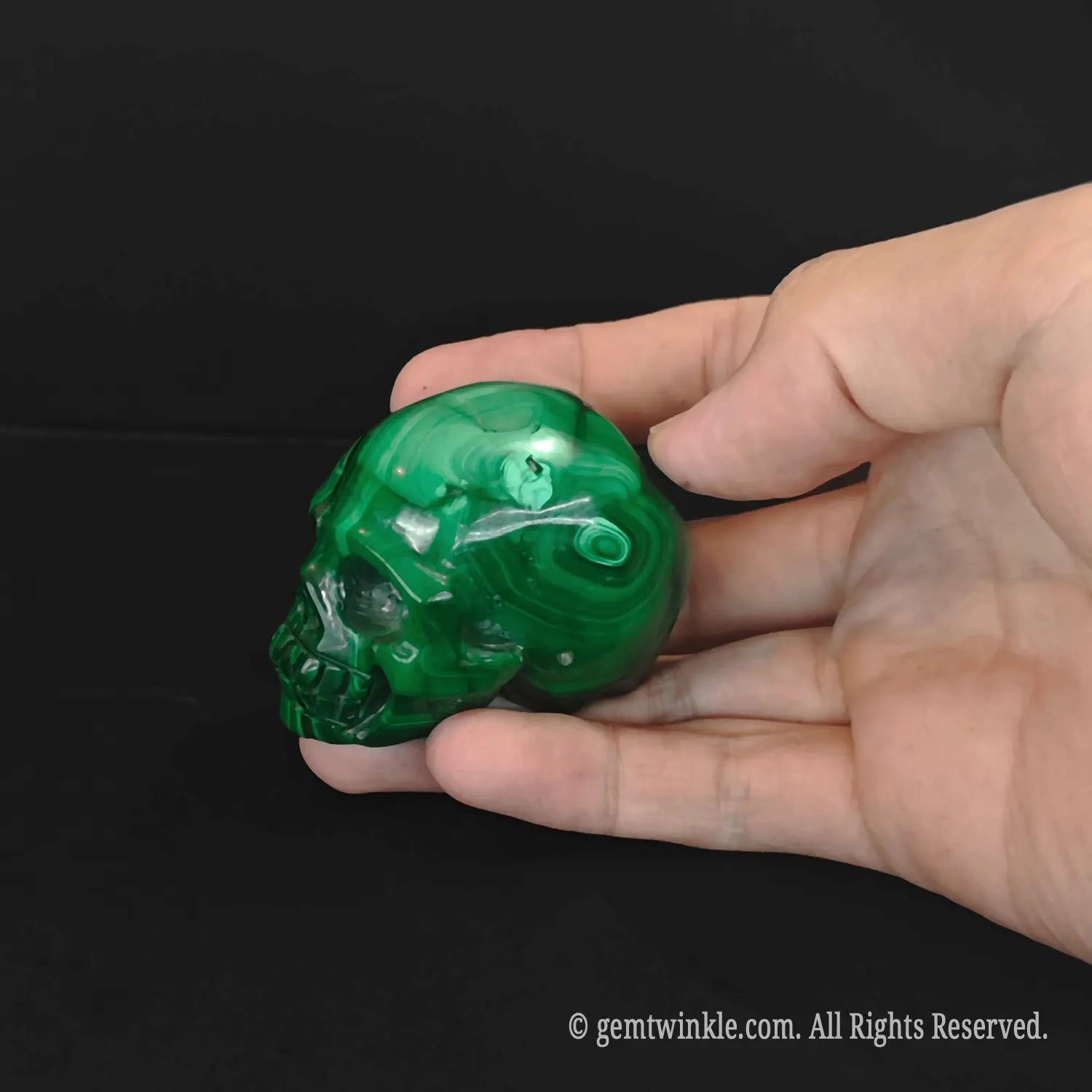 Side profile of a green malachite skull carving held in hand showcasing intricate natural mineral bands