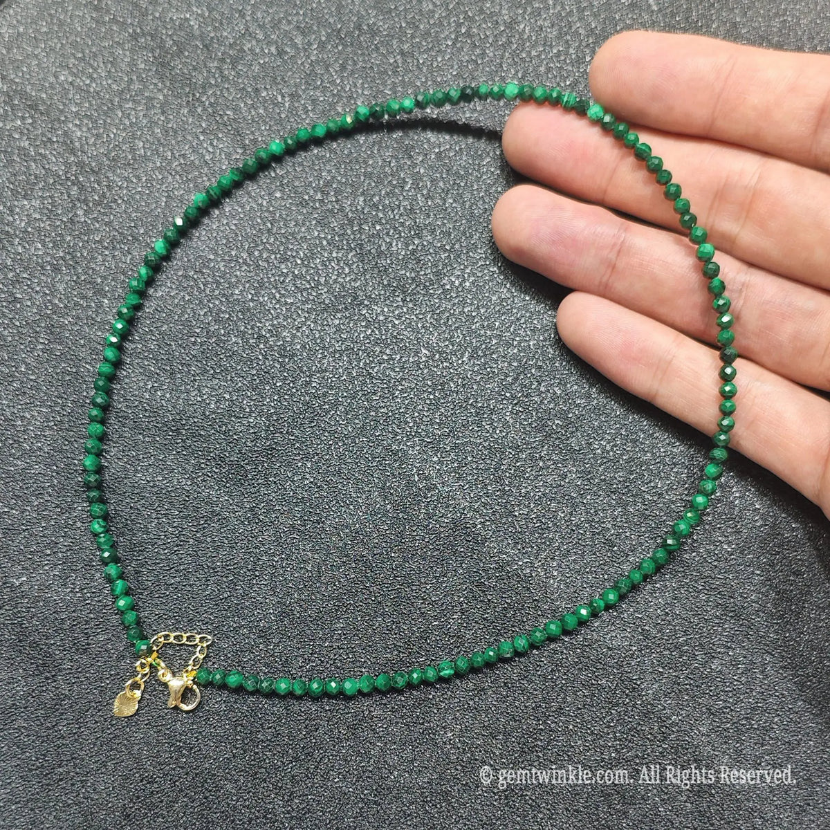 Hand holding 3mm faceted malachite necklace showing vivid forest green banding and gold clasp