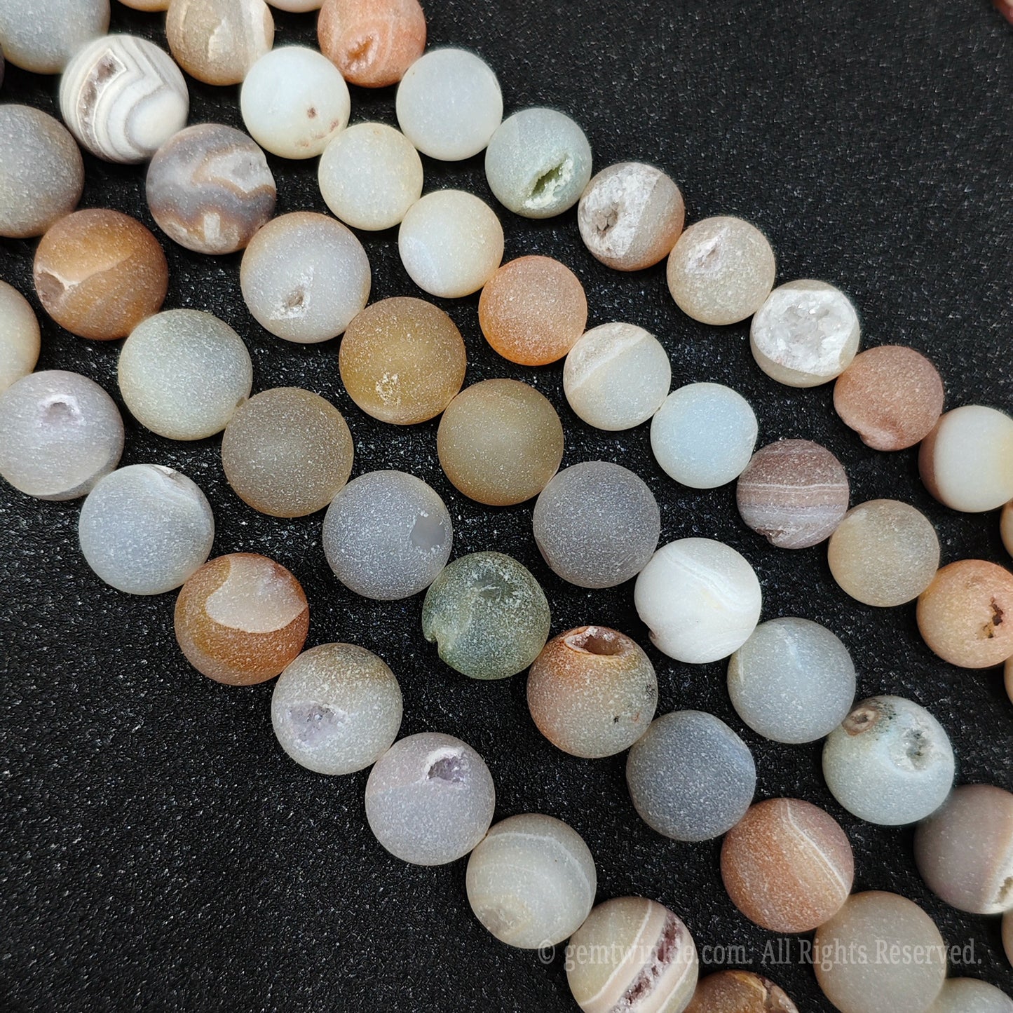 Detailed view of multiple matte agate stone beads with clear mineral banding and tiny sparkling druzy crystal pockets for jewelry making