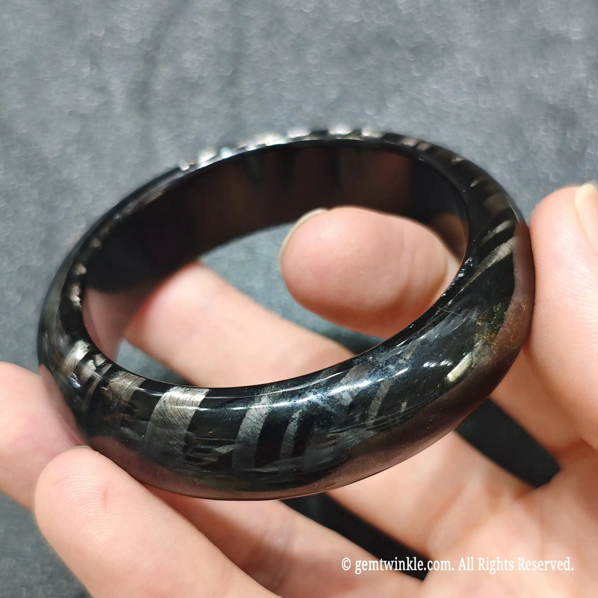 Close up view of metallic schiller hypersthene carved wristband showcasing parallel light-reflecting streaks